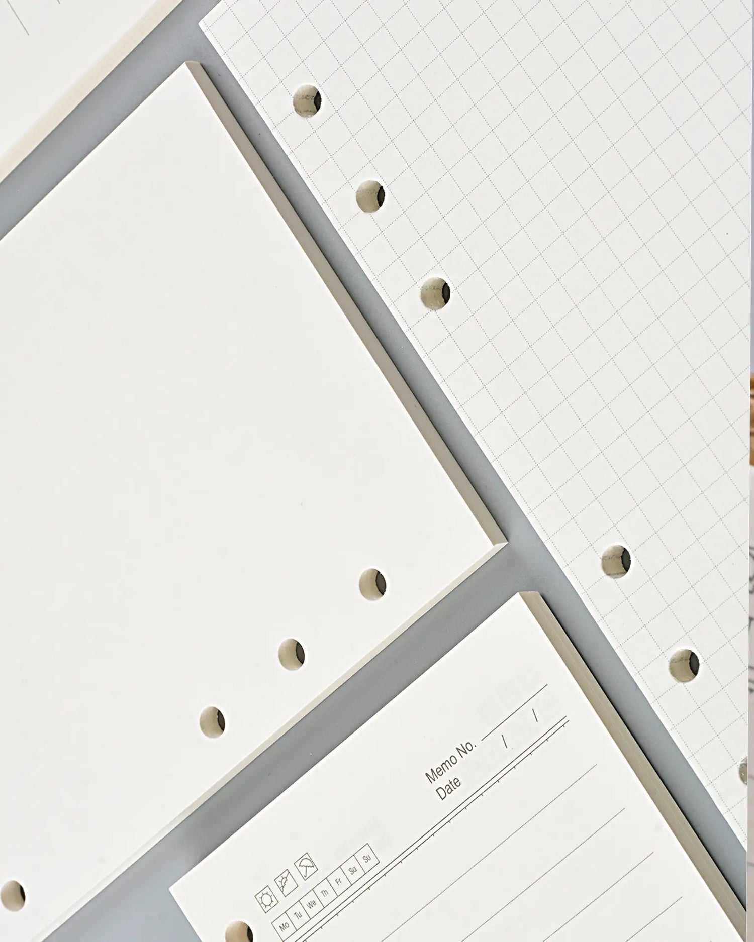 White and light gray hole-hole notebook paper and grid paper sheets arranged diagonally, showing the perforated edges and lined writing area.