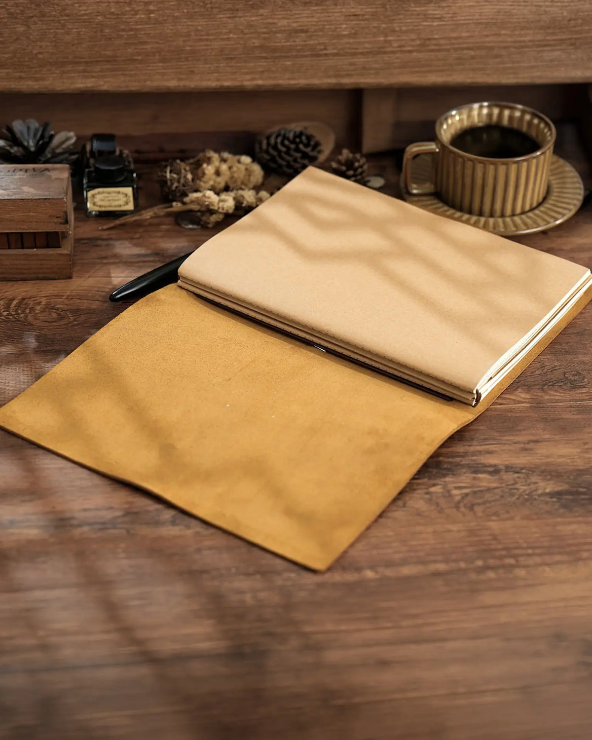 Open Cognac B5 refillable leather journal with notebook inserts on a wooden desk
