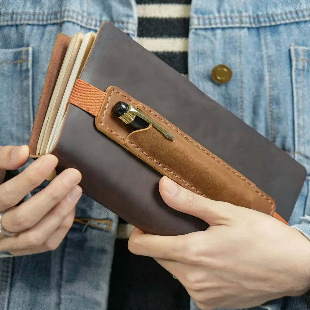 Brown leather pen holder attached to journal with elastic strap