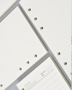 White and light gray hole-hole notebook paper and grid paper sheets arranged diagonally, showing the perforated edges and lined writing area.