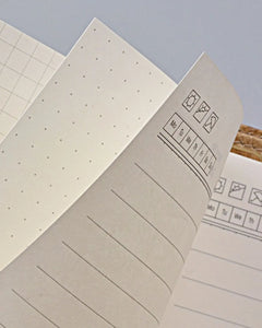 Close-up of open notebook pages showing dotted and lined writing paper with simple calendar and checklist icons on a pale blue background.