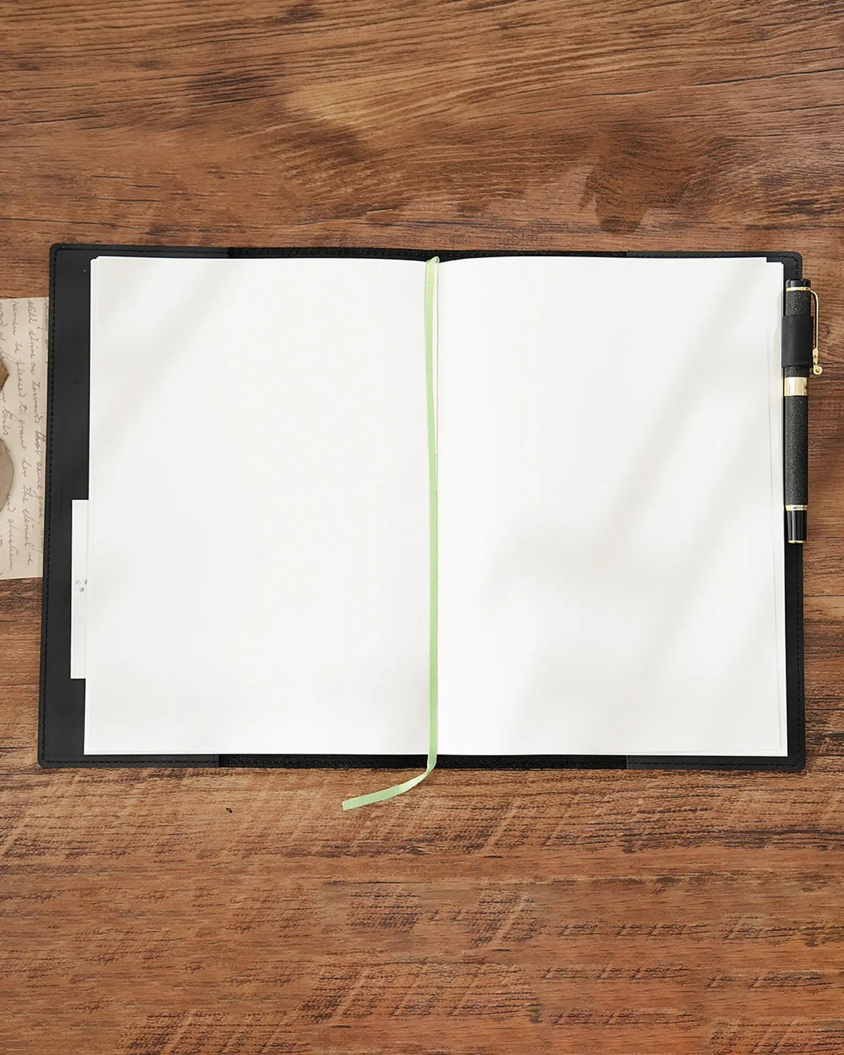 Black B5 refillable leather journal opened to blank pages with ribbon marker