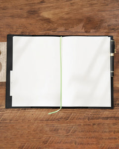 Black B5 refillable leather journal opened to blank pages with ribbon marker