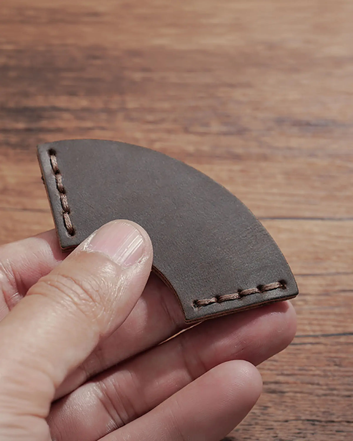 Close-up of a fan-shaped Espresso leather corner bookmark held in one hand