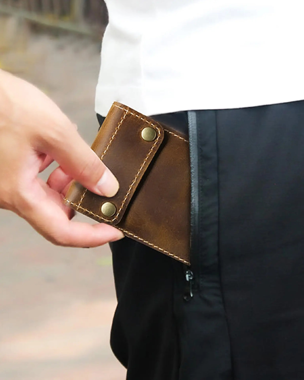 Person placing a closed brown watch sleeve into a trouser pocket