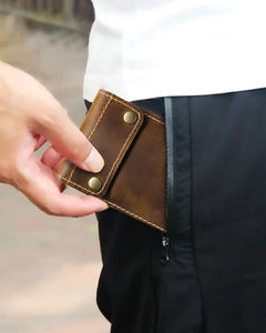 Person placing a closed brown watch sleeve into a trouser pocket