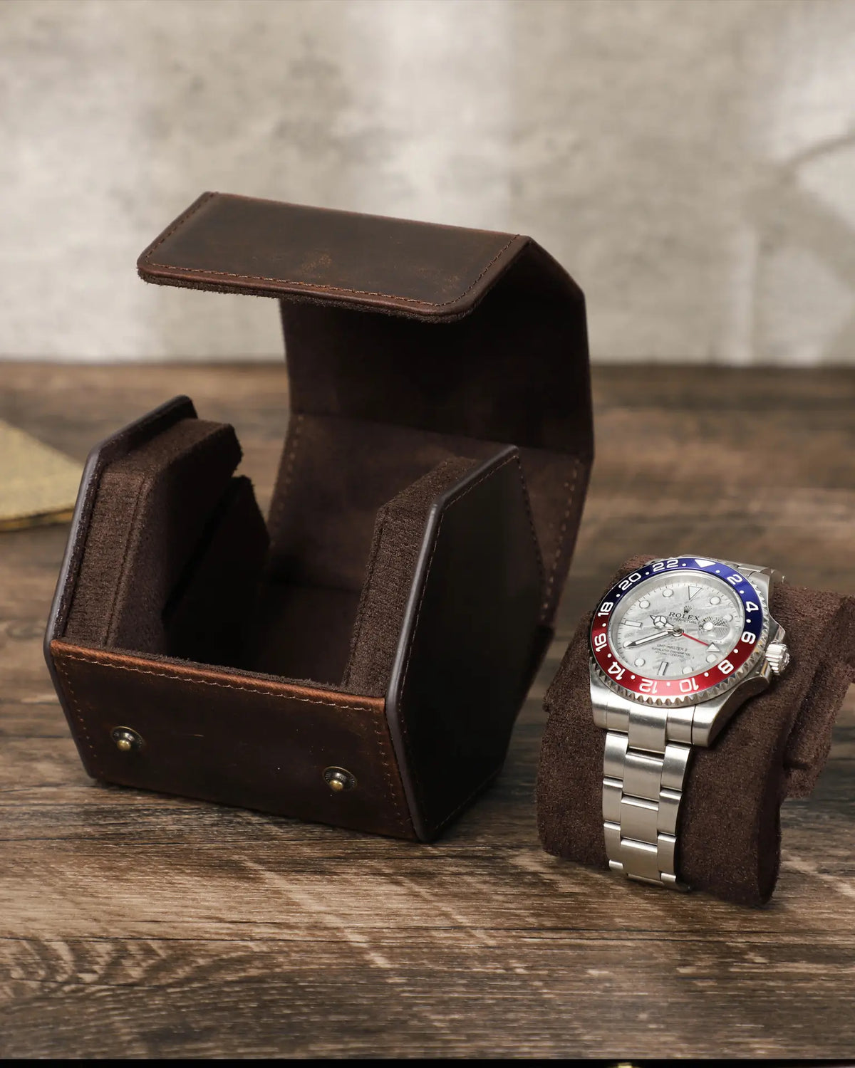 Open empty hex watch box beside a watch on its pillow