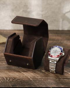 Open empty hex watch box beside a watch on its pillow