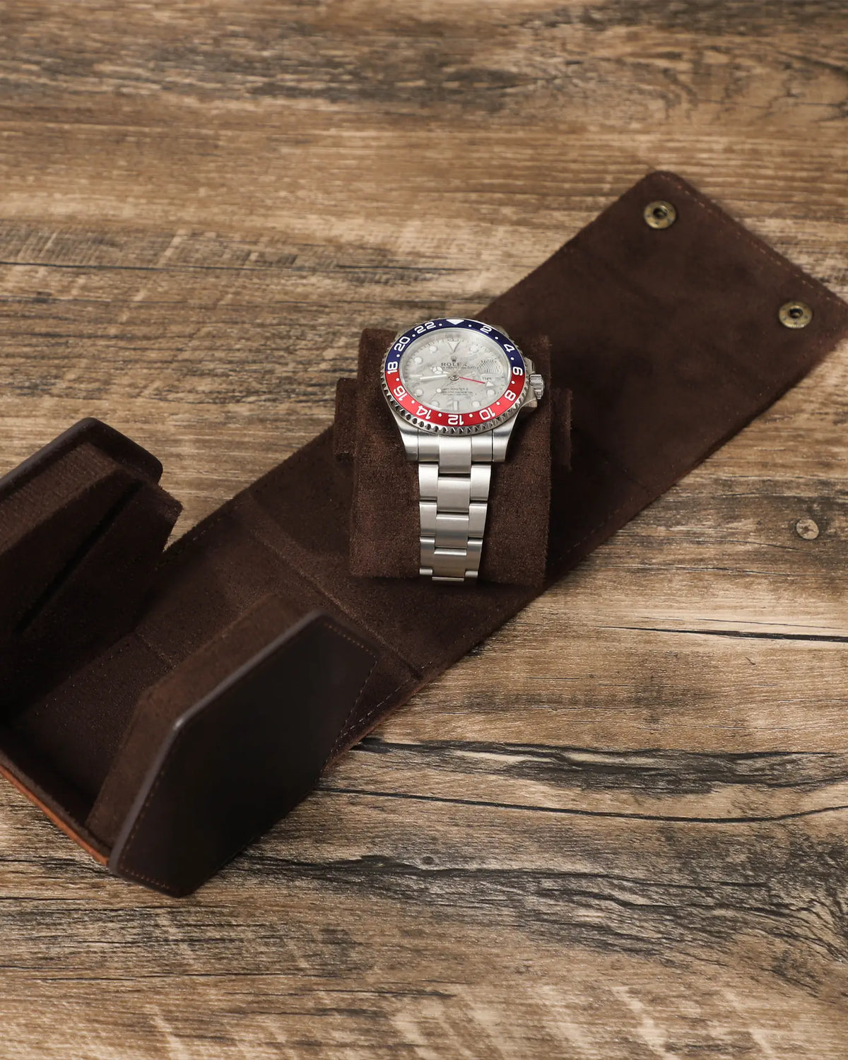 Open flattened watch box beside a watch on a removable pillow