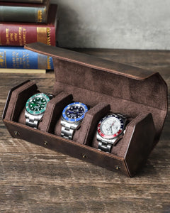 Open hex watch box holding three watches beside books