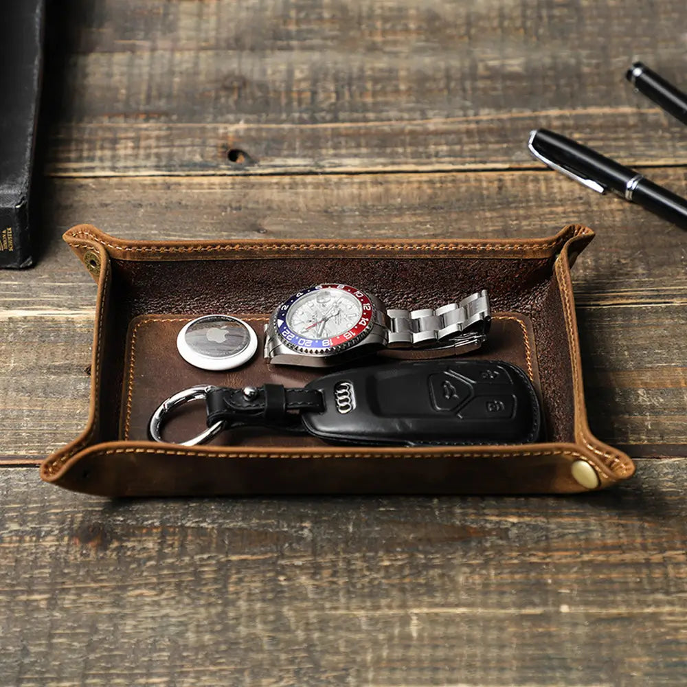 Brown leather tray with watch, keys, and coins on a wooden surface