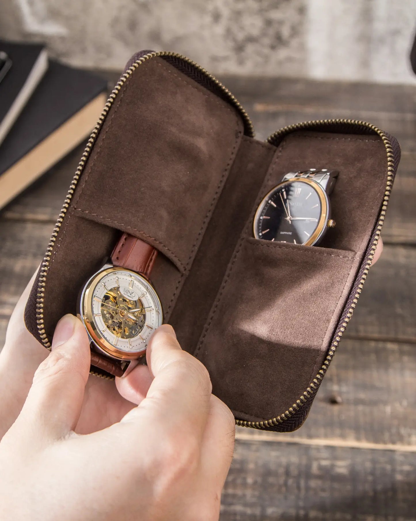 Hands placing watch into brown leather travel pouch with suede lined compartments