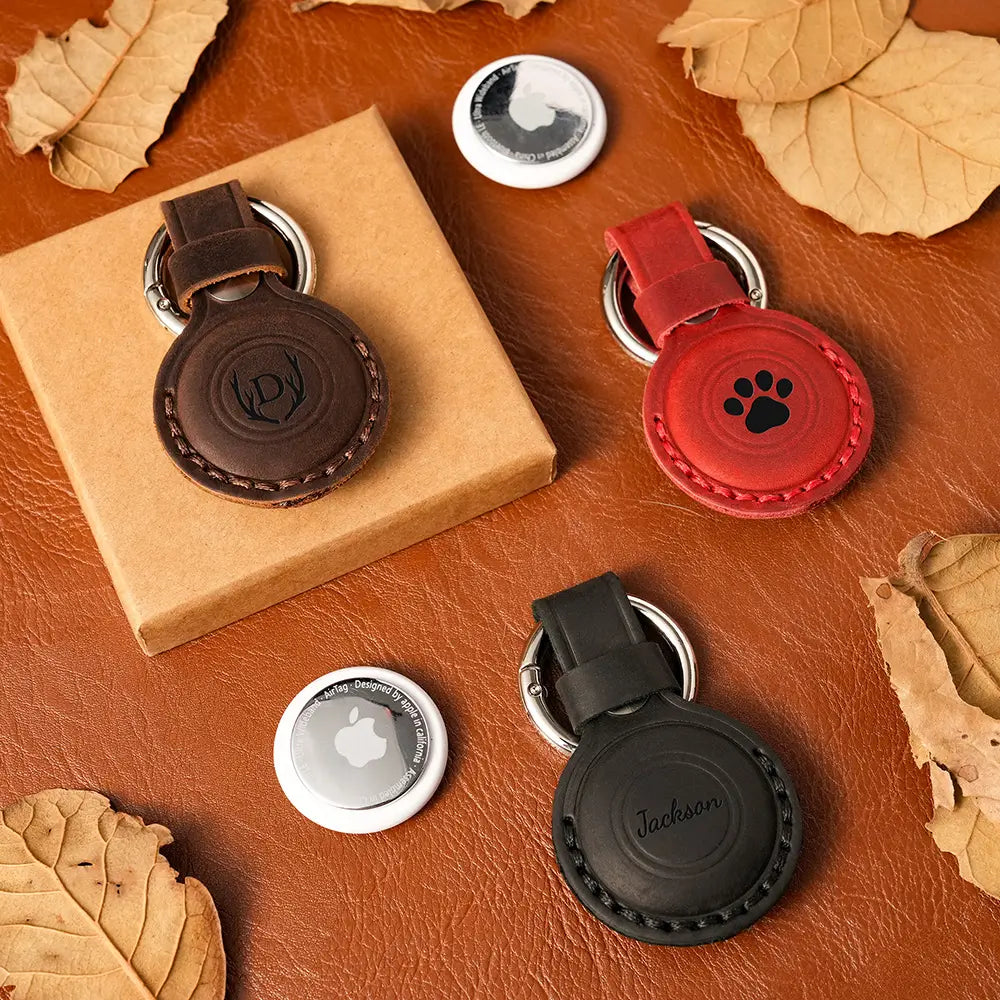 Four AirTag case on a brown leather surface with leaves.