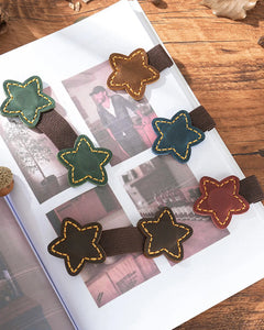 Star leather magnetic bookmarks with elastic pen loops displayed in five colors on an open book