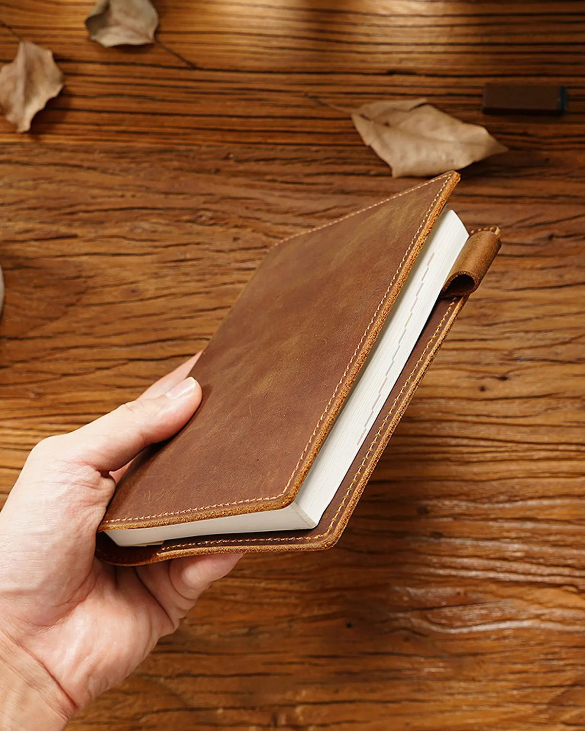 Cognac A6 leather writing folio shown in hand with notebook and pen loop