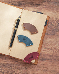 Personalized leather corner bookmarks with engraved monograms displayed on an open journal