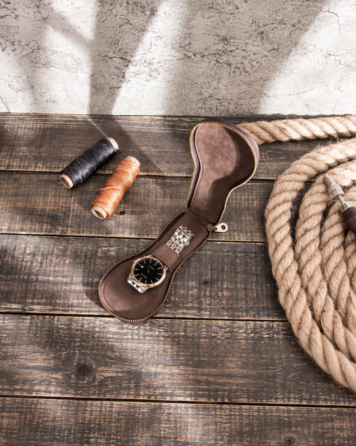 Top view of the open brown watch case with a watch on a wooden worktable.