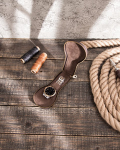 Top view of the open brown watch case with a watch on a wooden worktable.