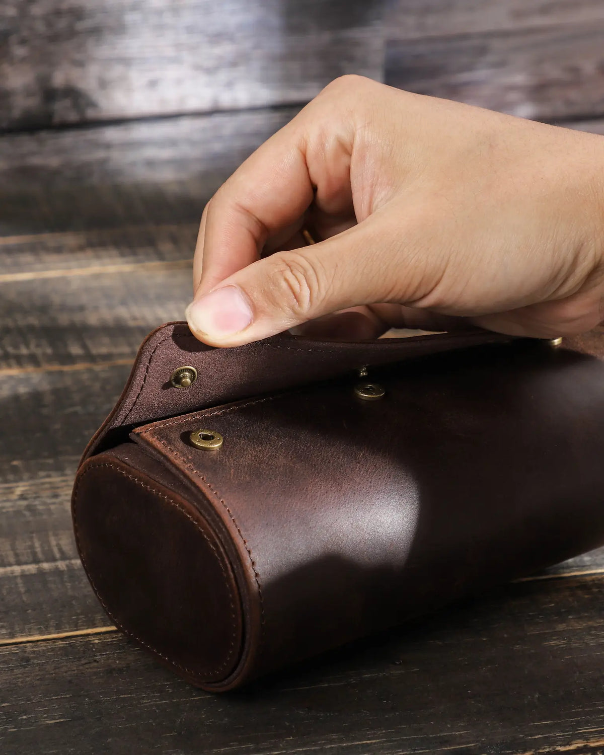 Close-up of a hand lifting the flap to show the hidden snap closure on the brown watch roll.