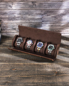 Brown four-watch roll open on a wooden table with four watches on separate cushions.