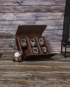 Brown six-watch case open on a wooden table with one watch cushion removed and placed beside it.