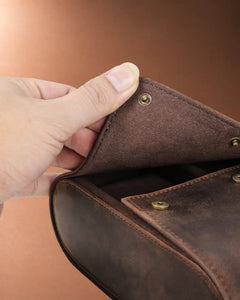 Close-up of a hand lifting the leather flap to show the hidden snap closure on the eight-watch case.