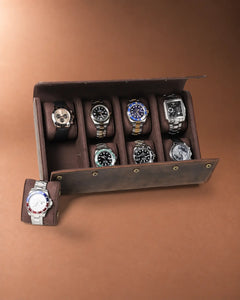 Open eight-watch case with seven watches inside and one watch on a removable cushion beside it.