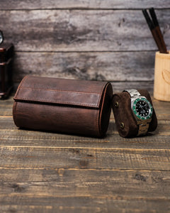 Closed brown double watch roll beside a removable cushion holding a metal-bracelet watch.
