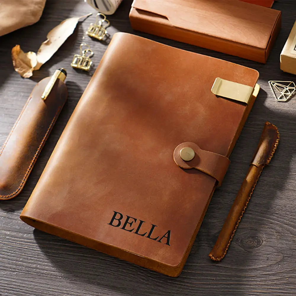 Brown leather notebook with 'BELLA' engraving on a wooden surface.