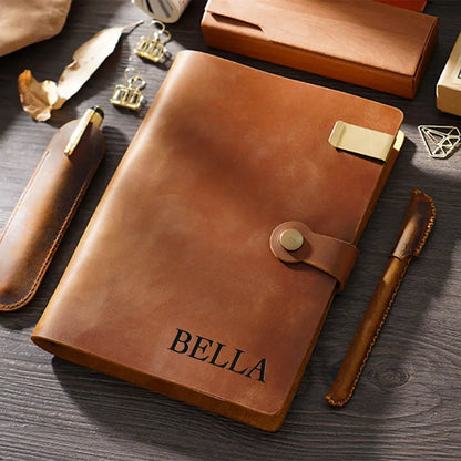 Brown leather notebook with 'BELLA' engraving on a wooden surface.