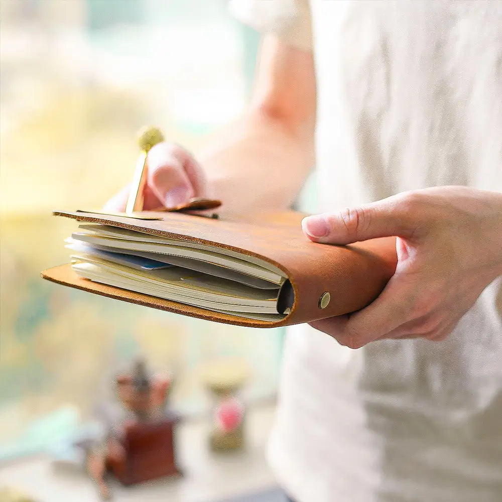 Person holding a brown leather notebook with a blurred indoor background