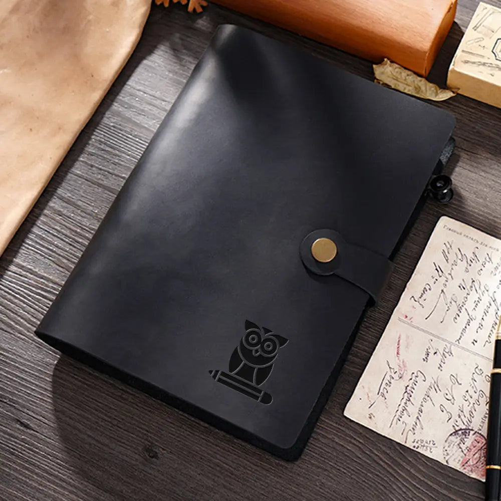 Black leather notebook with owl emblem on a wooden surface