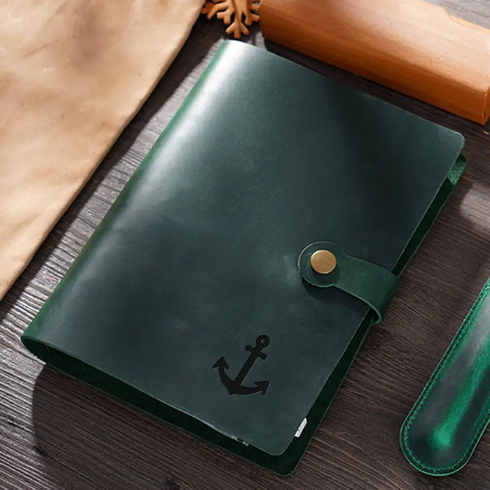 Green leather notebook with anchor emblem on a wooden surface
