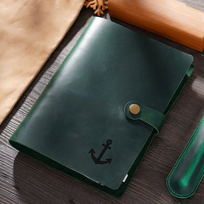 Green leather notebook with anchor emblem on a wooden surface