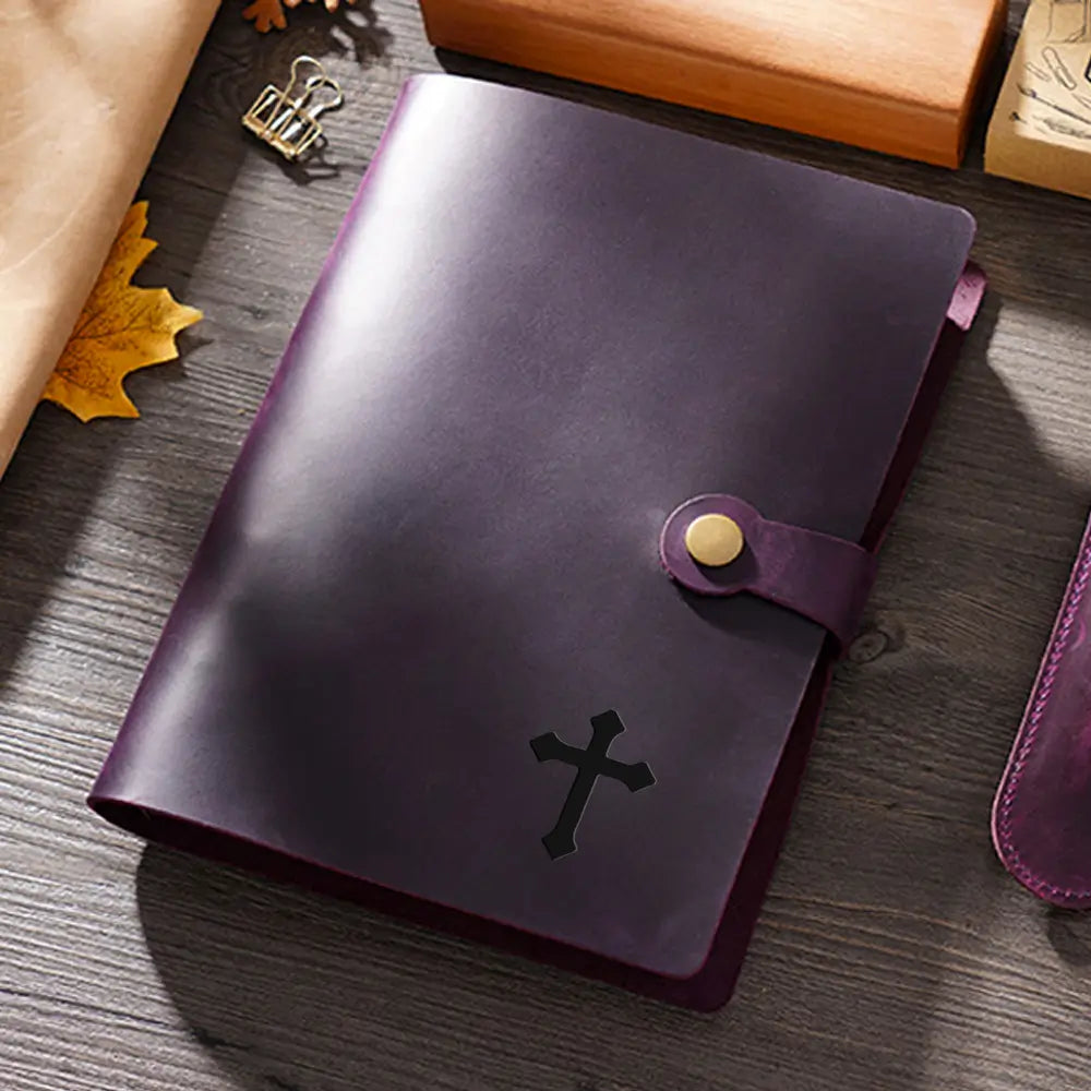 Purple leather notebook with a cross emblem on a wooden surface