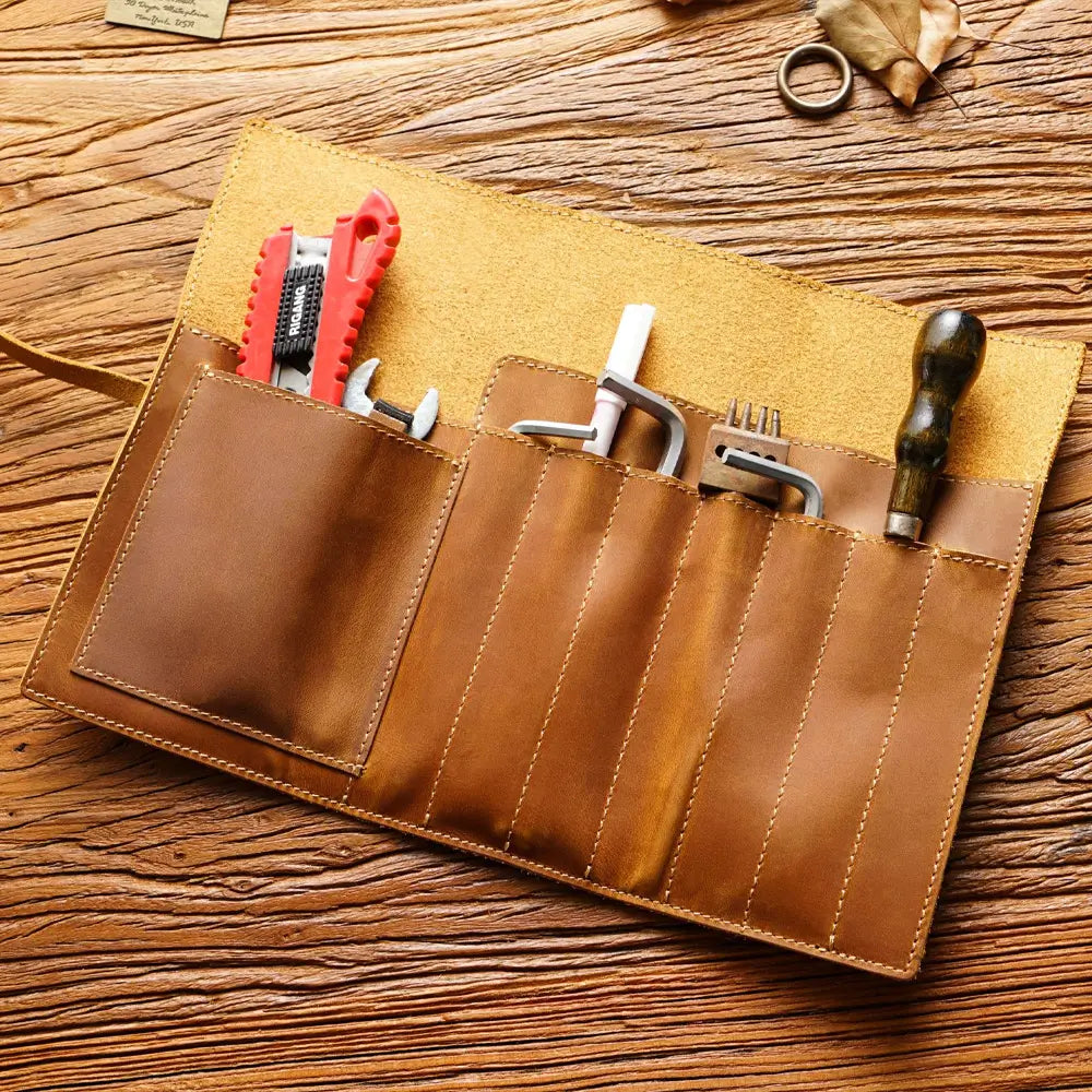 Brown leather tool roll with various tools on a wooden surface