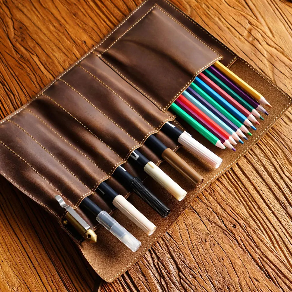 Brown leather pen and pencil holder with various pens and pencils on a wooden surface