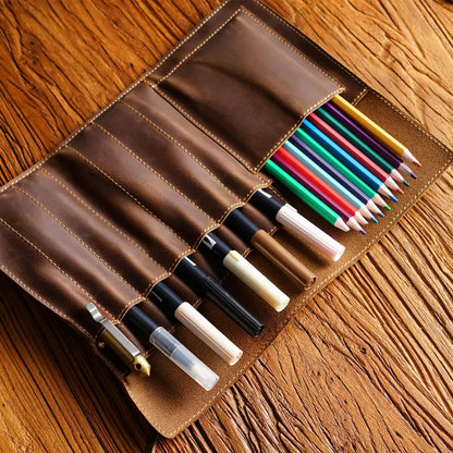 Brown leather pen and pencil holder with various pens and pencils on a wooden surface