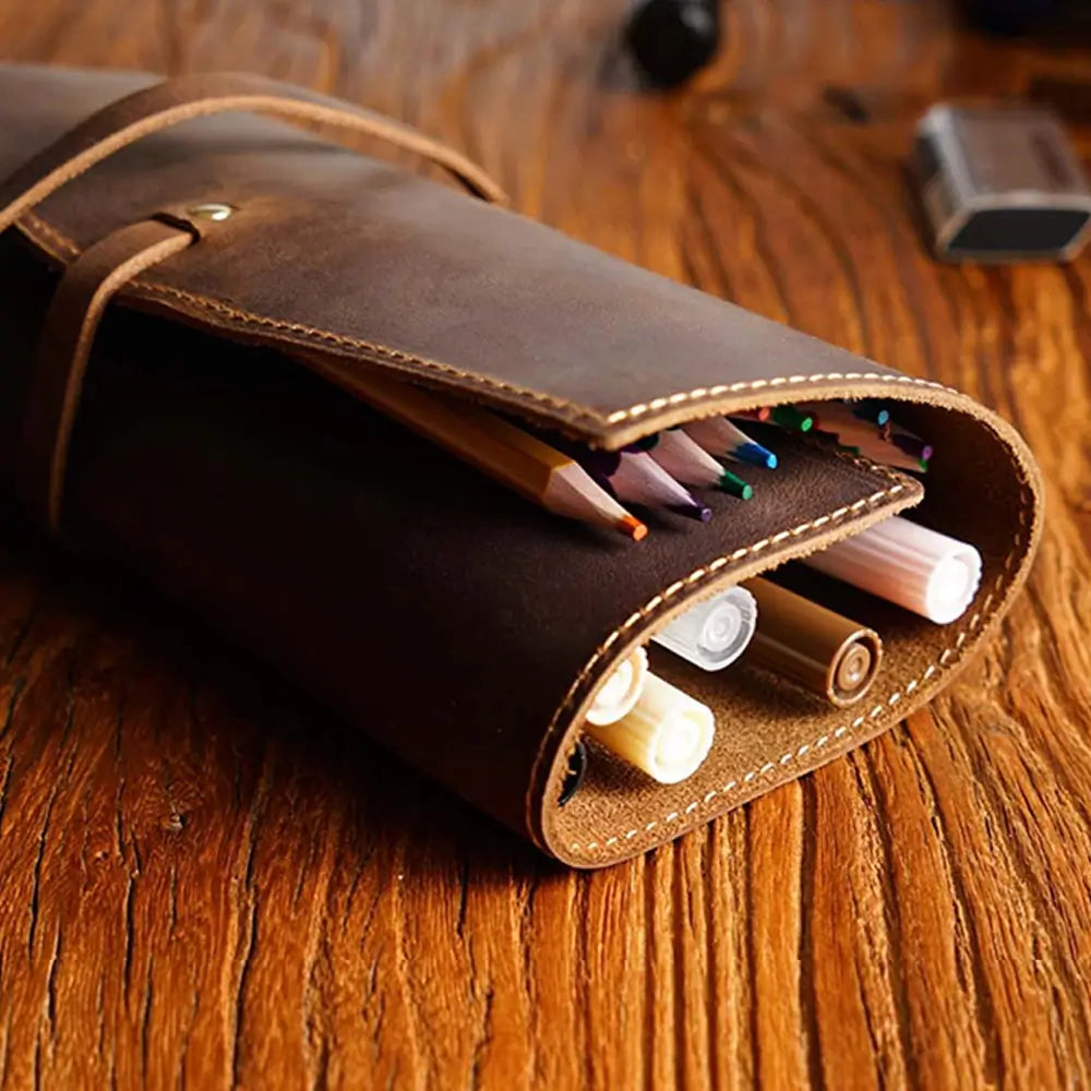 Brown leather pencil case with colored pencils and markers on a wooden surface