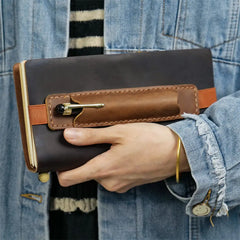Hand holding a brown leather notebook with a pen holder against a denim background