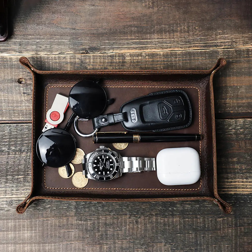 Leather valet tray with keys watch and coins on wooden surface